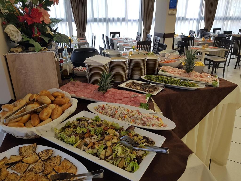 Bagātīgs bufetes galds ar dažādām uzkodām, salātiem un gaļas izstrādājumiem, kas rotāts ar ziediem un dekoratīviem traukiem. Ideāli piemērots svinībām vai pasākumiem.