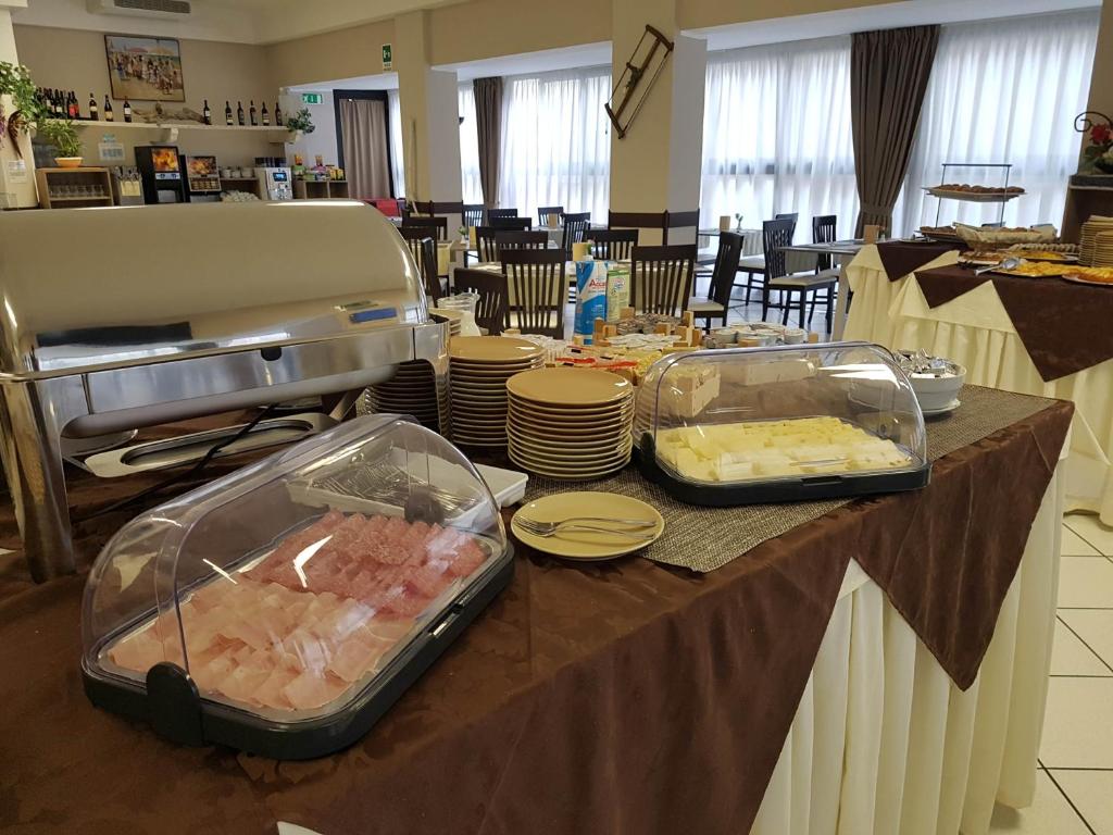 Bufete ar dažādiem ēdieniem, tostarp saldumiem un sieriem, izvietota restorānā ar gaišu interjeru. Galda klājums un ēdienu pasniegšanas stils rada viesmīlīgu atmosfēru.