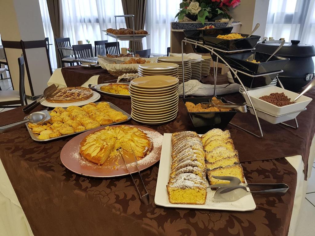 Bagātīgs desertu bufete ar dažādiem kārumiem, tostarp kūkām, cepumiem un maizēm, kas pasniegti uz galda ar dārziem un galdautu. Ideāls piedāvājums saldummīļiem.