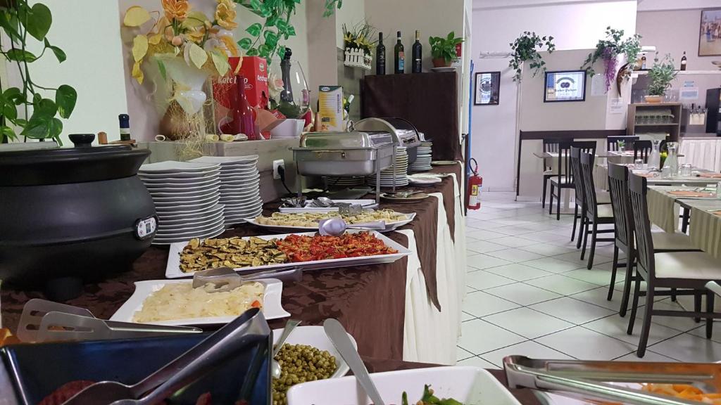 Svaigu ēdienu bufete ar dažādiem dārzeņiem un garnelēm, kas izvietota restorānā, kurā redzamas arī galdi un krēsli. Viegli zaļumi un dekorācijas piešķir mājīgu atmosfēru.