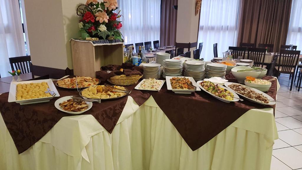 Bufete, kurā redzami dažādi ēdieni un uzkodas, ieskaitot salātus, maizes, gaļu un desertus. Galda apdare veidota ar brūnu galdautu un ziedu kompozīciju.