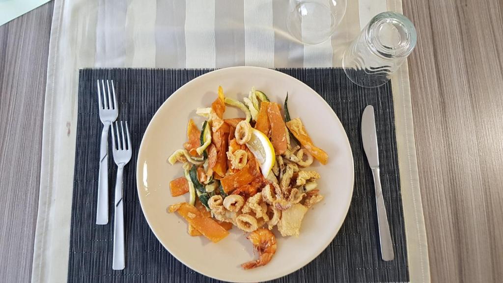 Ceļojošs jūras velšu ēdiens ar dārzeņiem, pasniegts uz šķīvja ar citronu. Uzkoda ir izkārtota uz eleganta galdauta ar galda piederumiem un glāzēm.