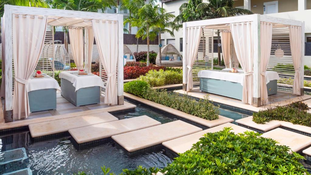 Spa procedūru zonas ar masāžas galdiem un mīkstām drānām, ieskautām zaļo augu un dārza ainavā.