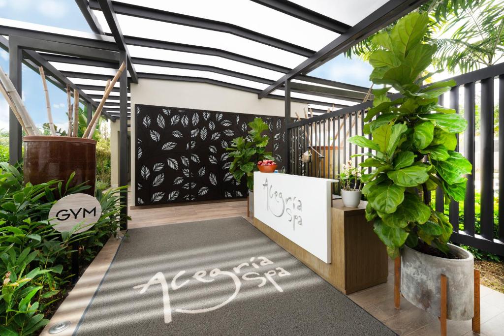 Mūsdienīgs spa uzņemšanas zona ar zaļām augu dekorācijām un stilīgu dizainu, kur redzama arī sporta zāles norāde.