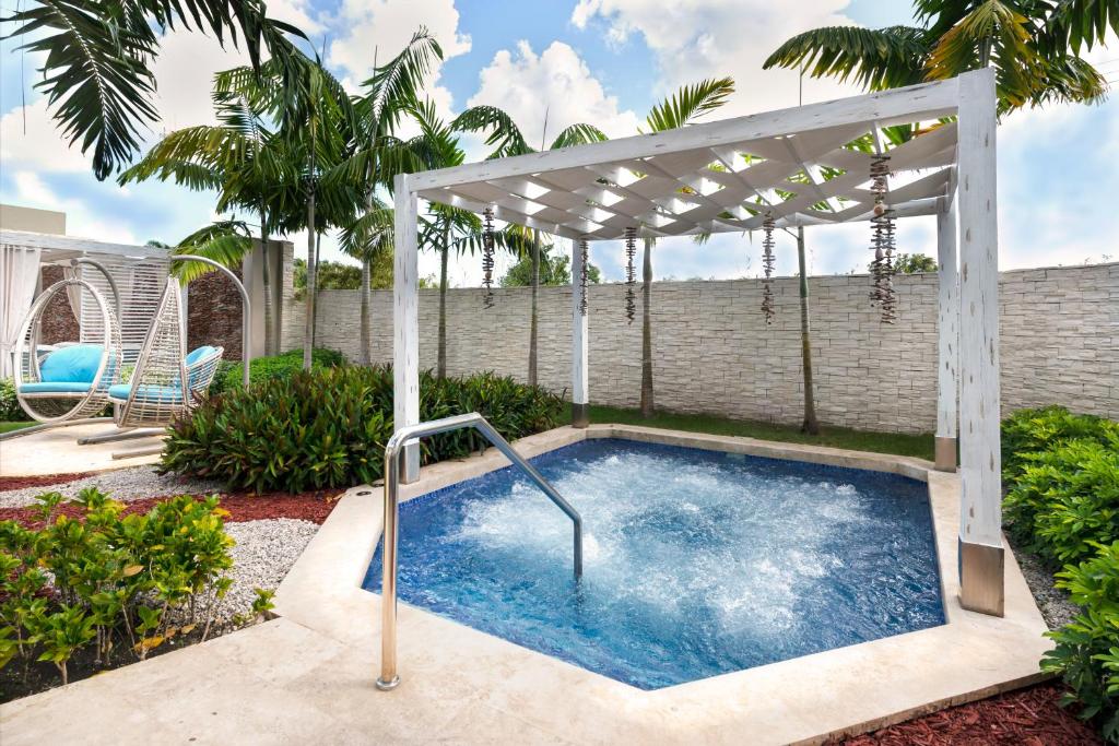 Dārza zona ar siltu ūdeni, ko ieskauj zaļumi un palmām, piedāvā relaksācijas vietu zem pergolas. Svaiga gaisa un komforta apvienojums.