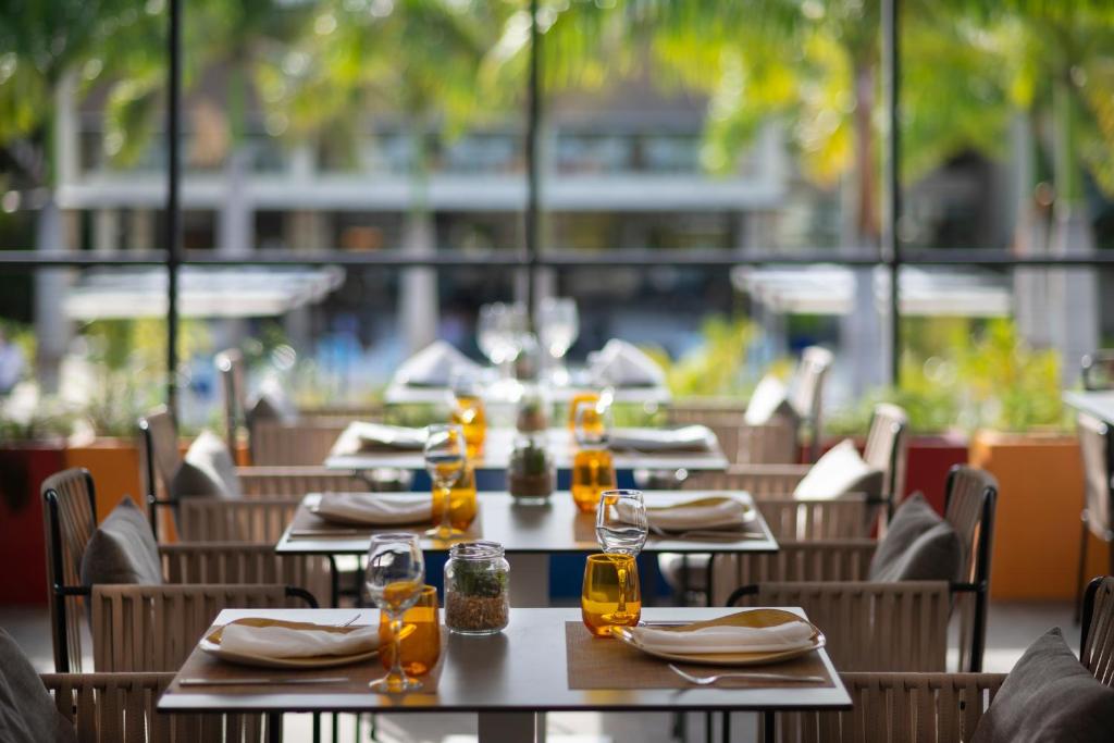 Mūsdienīgs restorāna interjers ar saulainu skatu, kur galdi ir sakārtoti ar elegantiem traukiem un dzērieniem, radot patīkamu atmosfēru.