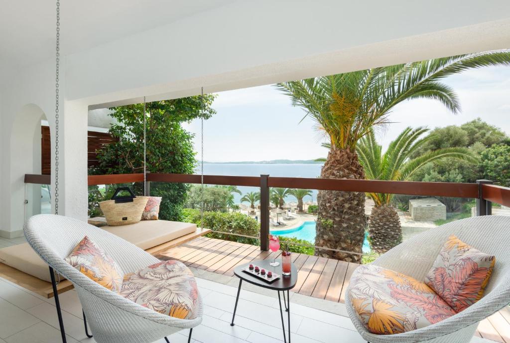 Mūsdienīgs balkons ar skatu uz jūru, kurā ir ērtas šūpuļkrēslas un galdiņš ar dzērieniem. Apkārt palmām un zaļumiem, radot relaksējošu atmosfēru.