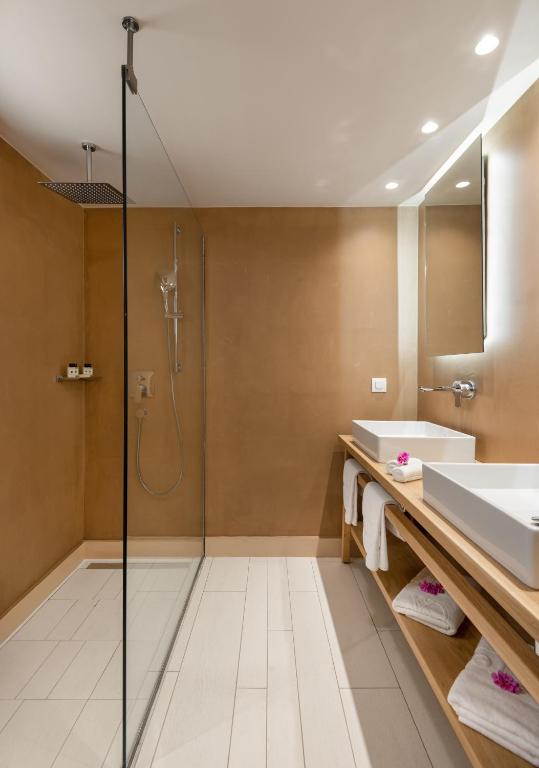 Mūsdienīga vannas istaba ar stikla dušu, koka izlietni un elegantu apgaismojumu. Sienas ir krāsotas siltā tonī, radot relaksējošu atmosfēru.