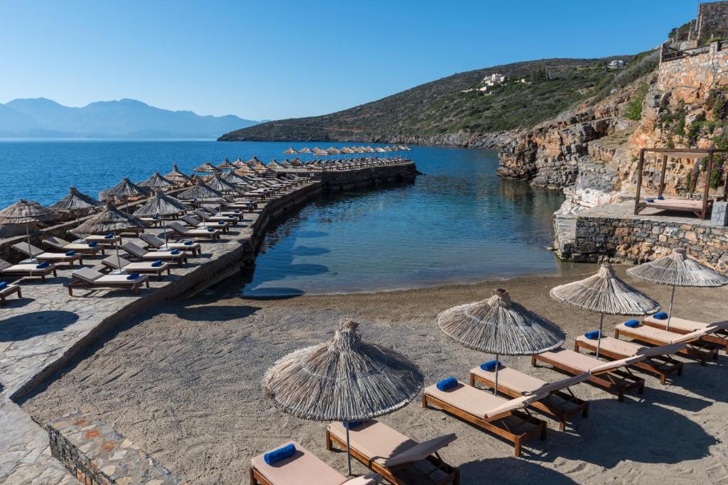 Aquila Elounda Village piekrastes atpūtas zona ar sauļošanās krēsliem un lietussargiem
