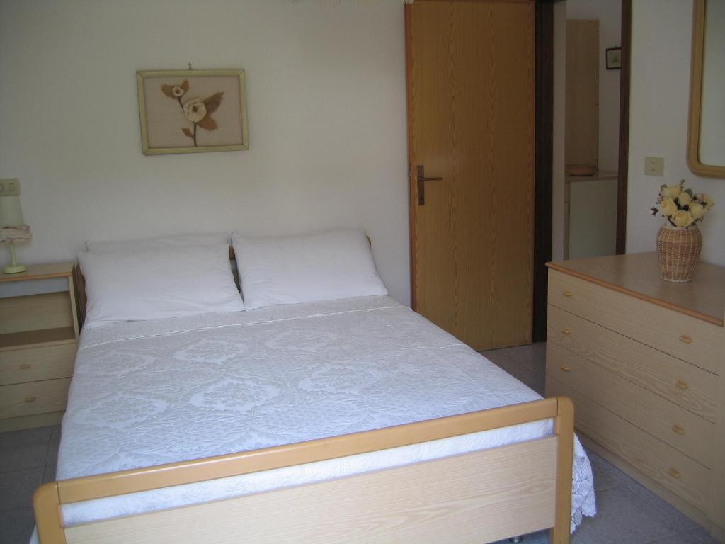 Mūsdienīga guļamistaba ar divguļamo gultu, koka mēbelēm un gaismas toņiem. Telpā ir arī dekoratīvs attēls un ziedu kompozīcija uz galda.