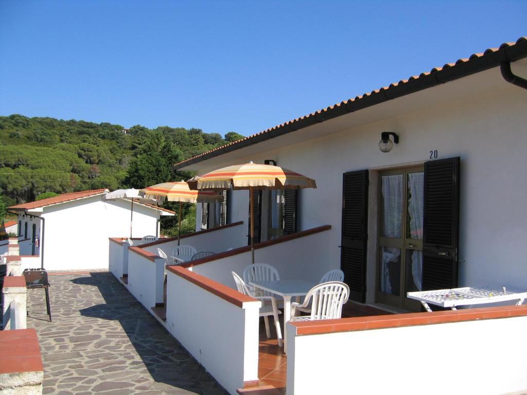 Vasaras māju komplekss ar terasēm un saulessargiem, kas izvietots gleznainā apkārtnē. Skats uz zaļajiem pakalniem un skaidro zilo debesu fonu.