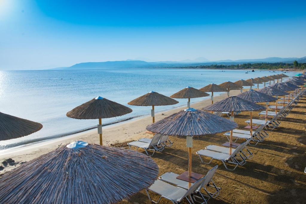 Pludmales skats ar sauļošanās krēsliem un salmiem, kas novietoti gar piekrasti, un mierīgu jūru fonā. Ideāla vieta relaksācijai un atpūtai.