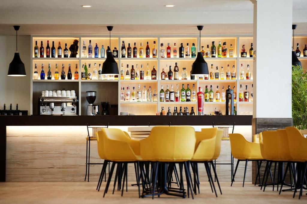 Mūsdienīgs bārs ar plašu dzērienu izvēli un dzeltenām krēsliem, kas nodrošina komfortablu sēdvietu. Bāra plauktos ir redzamas dažādas alkoholiskās un bezalkoholiskās dzērienu pudeles.