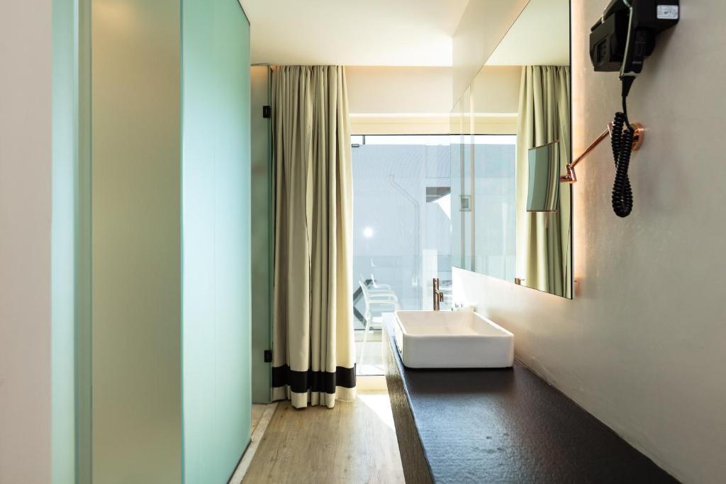 Mūsdienīgs vannas istabas interjers ar gaiši zaļu sienu, elegantām drānām un minimālistisku izlietni uz melna darba virsmas. Gaisma ieplūst caur lieliem logiem, radot patīkamu atmosfēru.