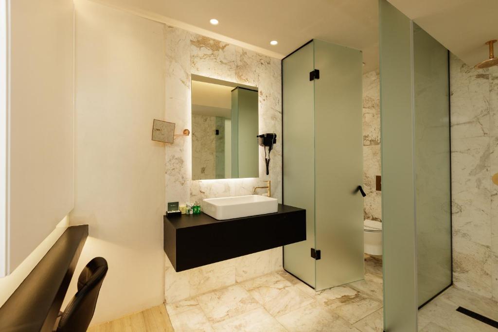 Mūsdienīgs vannas istabas interjers ar akmens tekstūru, pelēku un melnu krāsu kombināciju, kā arī stikla dušas kabīni un elegantu izlietni.