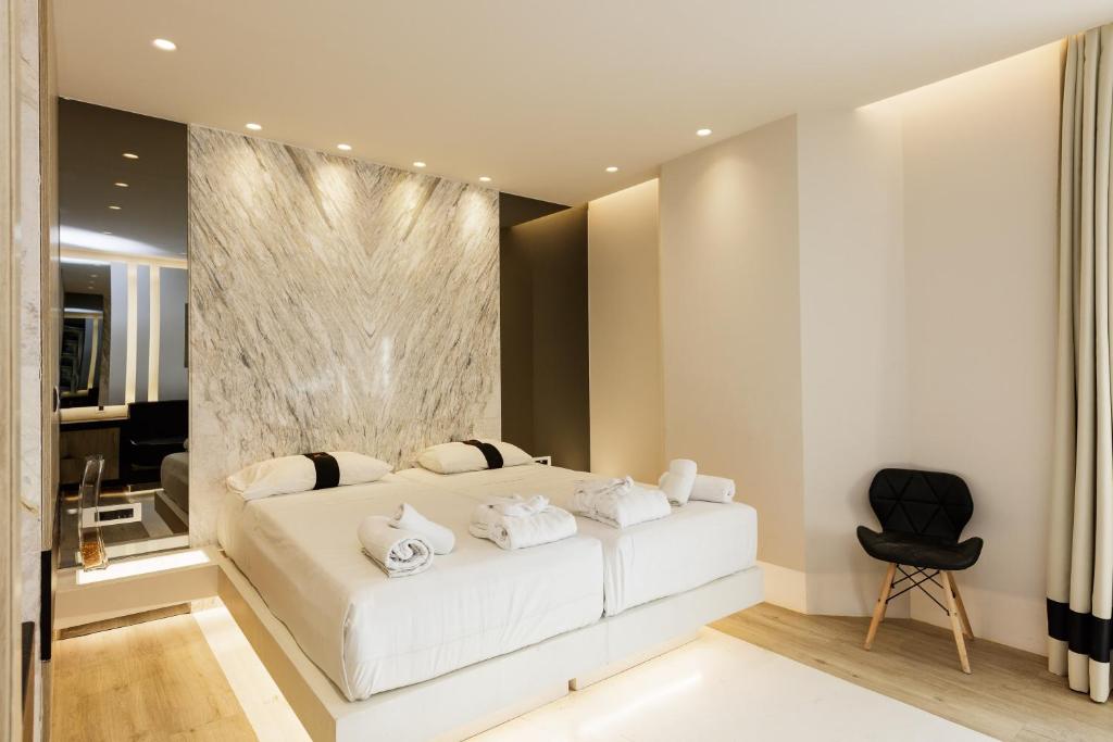 Mūsdienīgas guļamistabas iekārtojums ar divguļamo gultu, elegantu akmens sienu un minimālistisku dizainu. Telpā ir ērta krēsla un mīksto tekstilizstrādājumu elementi.