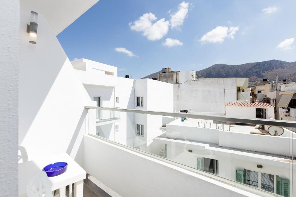 Balcony view featuring modern white architecture and a clear blue sky, with a backdrop of mountains and a few scattered clouds. A small table with a blue bowl adds a touch of detail to the serene setting.