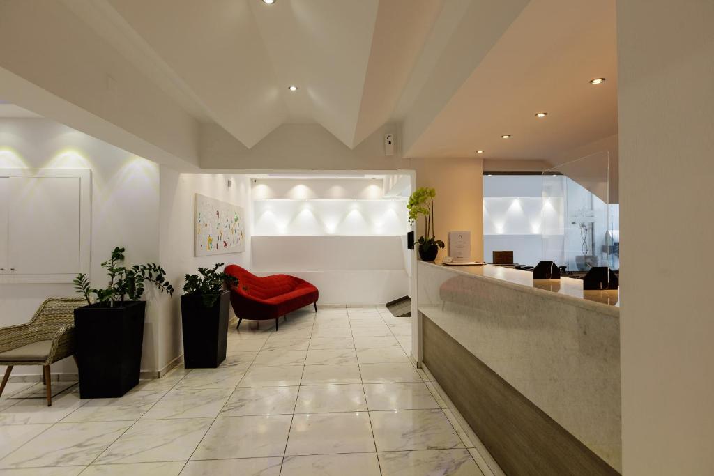 Mūsdienīgs viesnīcas reģistratūras interjers ar elegantu balto sienu apdari, marmora grīdu un sarkanu dīvānu. Interjērā redzami augi un mākslas darbs uz sienas, radot viesmīlīgu atmosfēru.