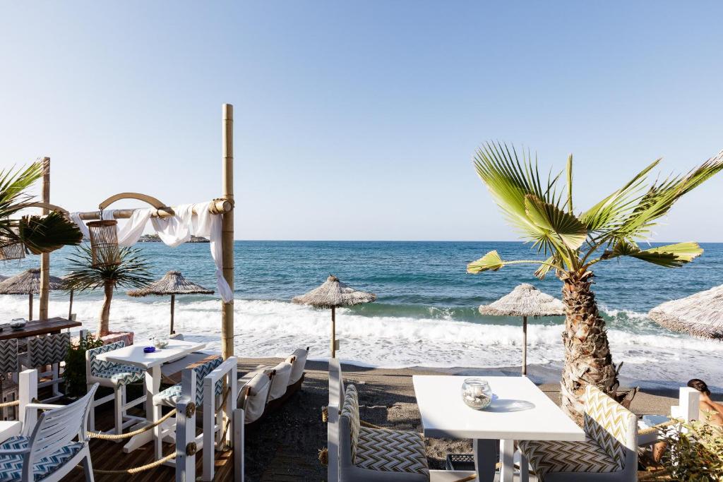 Pludmales restorāna terase ar skatu uz jūru, palmām un saulessargiem, kas sniedz relaksējošu atmosfēru. Ideāla vieta atpūtai pie ūdens.