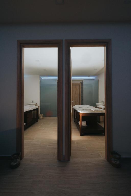 Divas relaksējošas masāžas telpas ar koka durvīm, apgaismotas ar siltu gaismu, radot mierīgu atmosfēru. Telpās ir masāžas galdi un mūsdienīgs dizains.