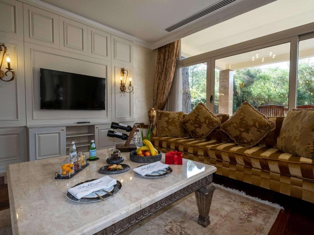 Luksusa viesnīcas numurs Rixos Premium Belek ar ērtu dīvānu un augļiem uz galda.