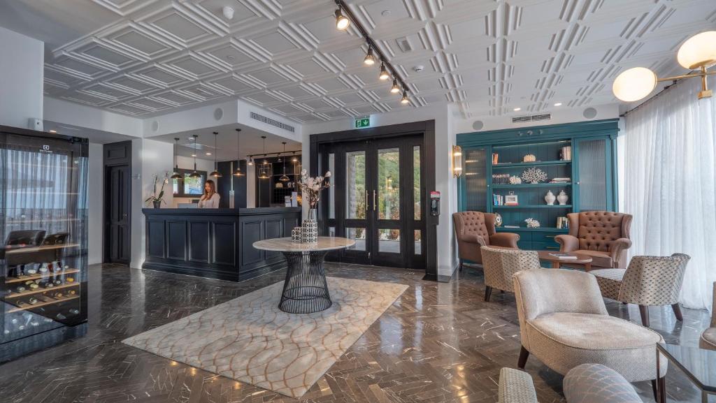 Mūsdienīgs viesnīcas recepcijas interjers ar elegantu dekoru, reģistratūru un komfortablām sēdvietām. Telpā ir gaišas krāsas un stilīgas gaismas, radot viesmīlīgu atmosfēru.