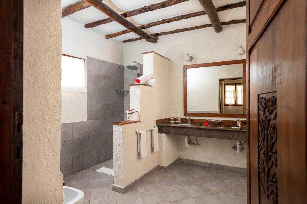 Moderns vannas istabas dizains ar dabīgām koka sijām, plašu spoguli un elegantu dušas zonu. Svaigi ziedi pie izlietnes piešķir mājīgumu un greznību.