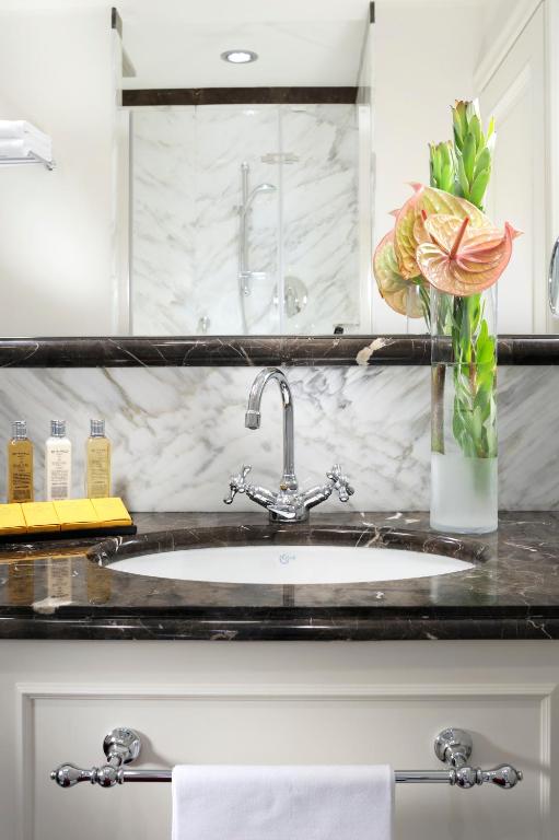 Elegants vannas istabas interjers ar marmora virsmu, modernu jaucējkrānu un ziedu kompozīciju. Uz letes izvietoti higiēnas produkti un dvielis.