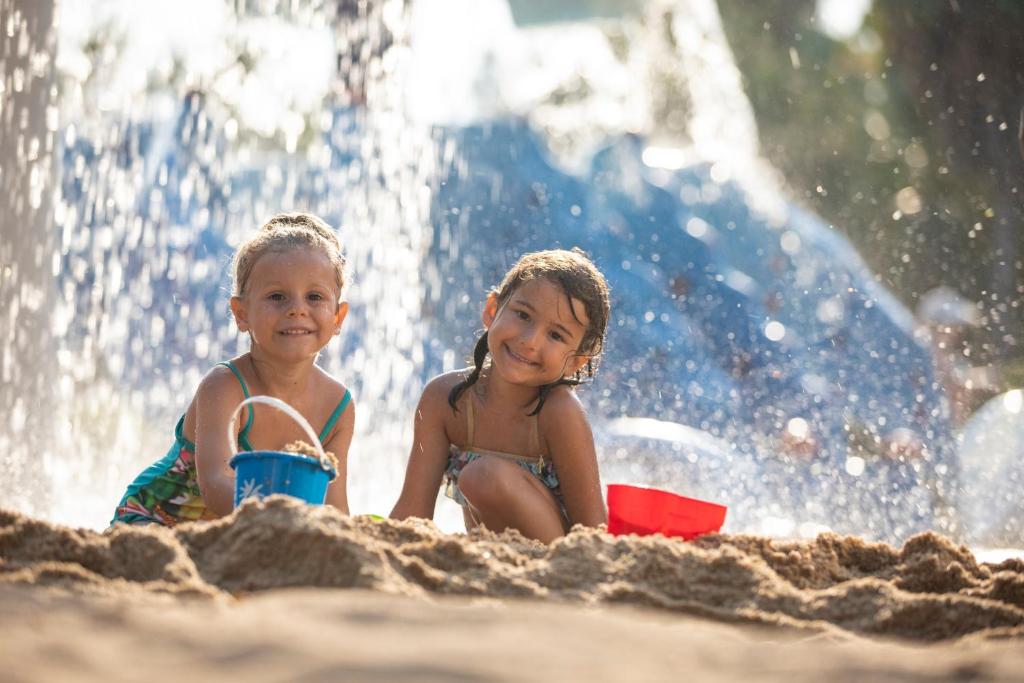 Divas laimīgas meitenes spēlē smilšainā pludmalē pie Ali Bey Club.