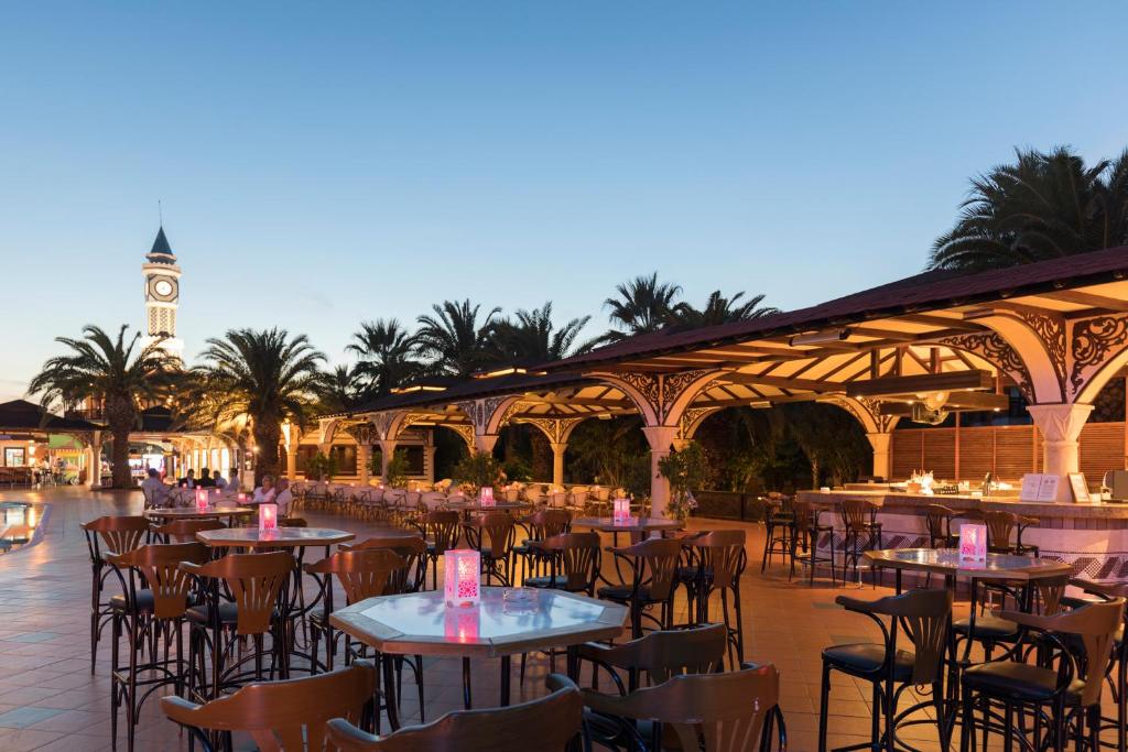 Ārējā restorāna zona pie Ali Bey Club ar palmām un apgaismojumu saulrieta stundā.