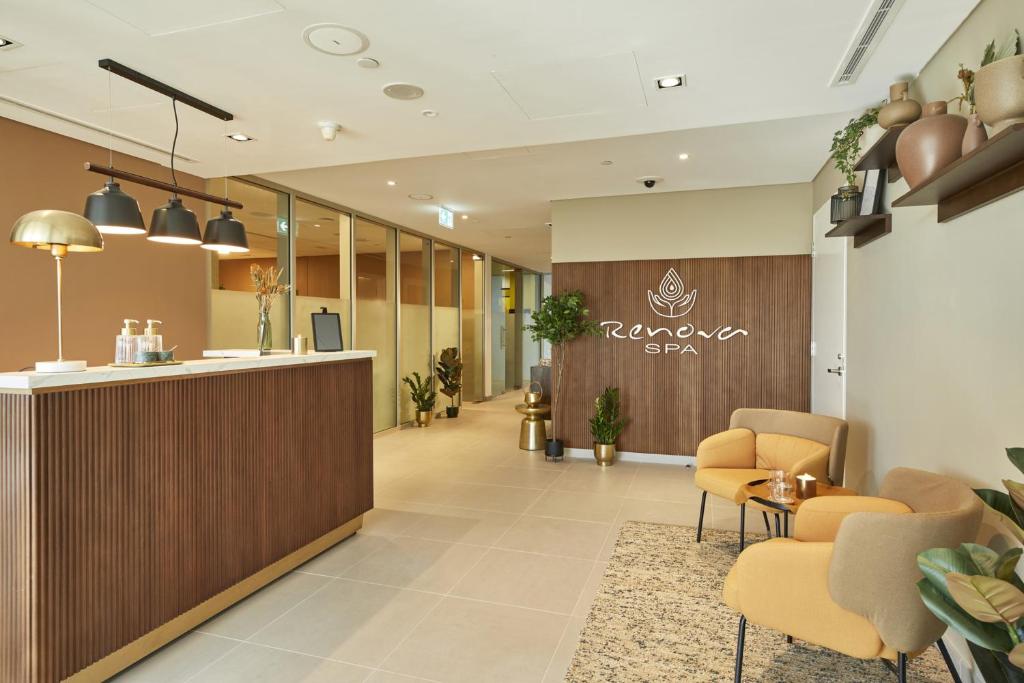 Mūsdienīgs spa reģistratūras interjers ar siltām krāsām, dabiskiem akcentiem un ērtām sēdvietām. Uz sienas redzams "Renova SPA" zīmols, kas rada relaksējošu atmosfēru.