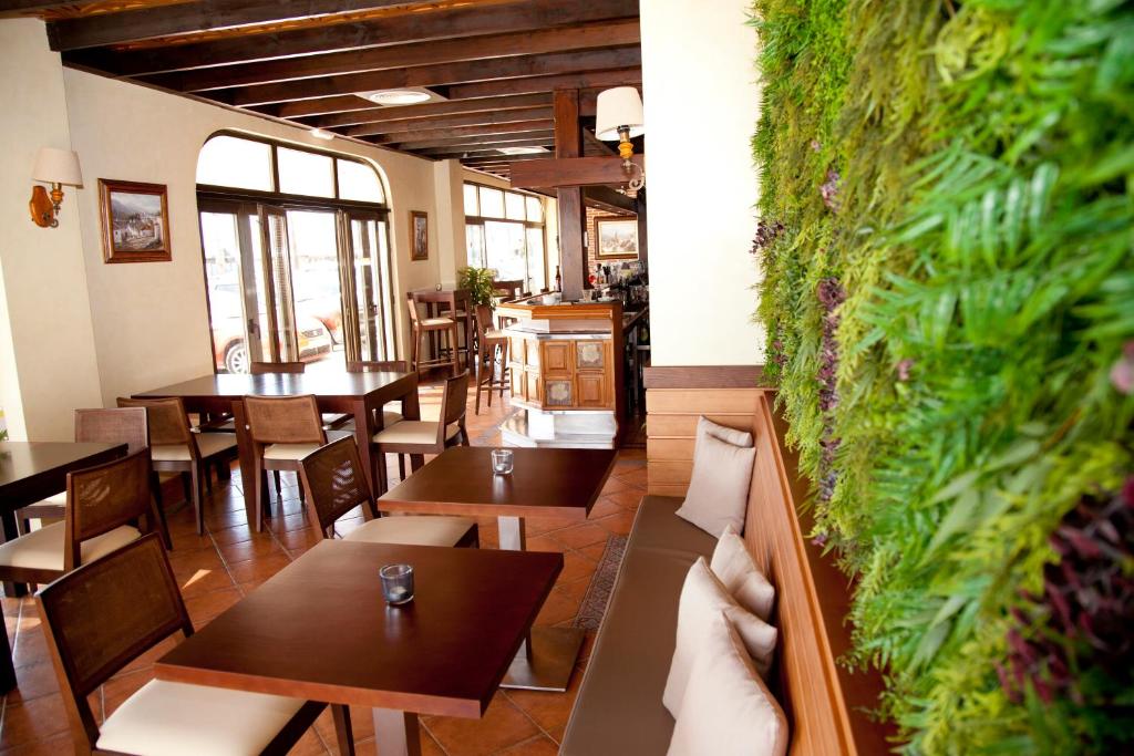 Mūsdienīga restorāna interjers ar koka griestiem un zaļumu sienu, kas rada patīkamu atmosfēru. Telpā ir dažādas ēdamvietas un bārs, kas aicina uz relaksāciju un baudīšanu.