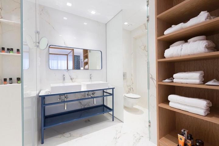 Mūsdienīgs vannas istabas dizains ar diviem izlietnēm, stikla dušu un elegantu koka plauktu ar dvieļiem un kosmētiku.