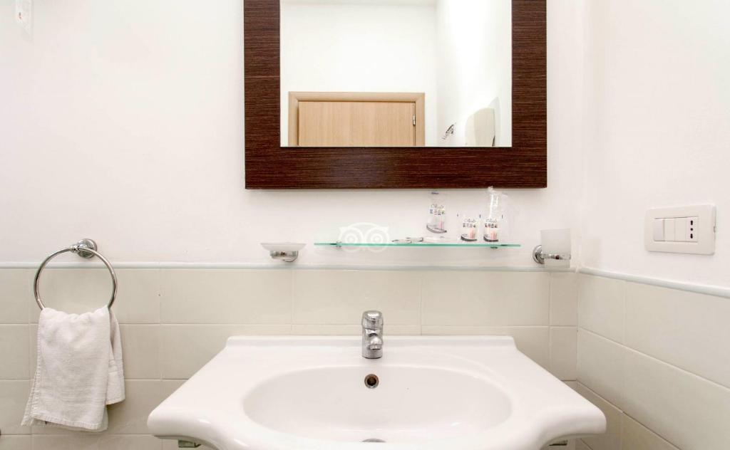 Mūsdienīgs vannas istabas izskats ar baltu izlietni, spoguli un tīru, minimālistisku dizainu. Vannas istabā ir pieejami pamata higiēnas piederumi un dvielis.