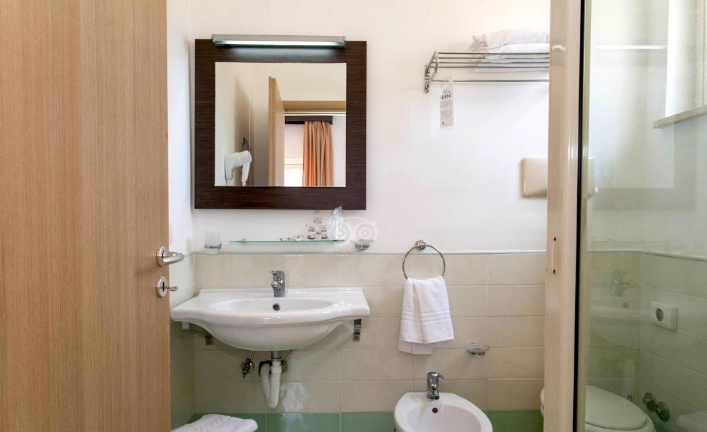 Mūsdienīga vannas istaba ar baltu izlietni, spoguli un higiēnas piederumiem, kas radījusi tīru un ērtu atmosfēru.