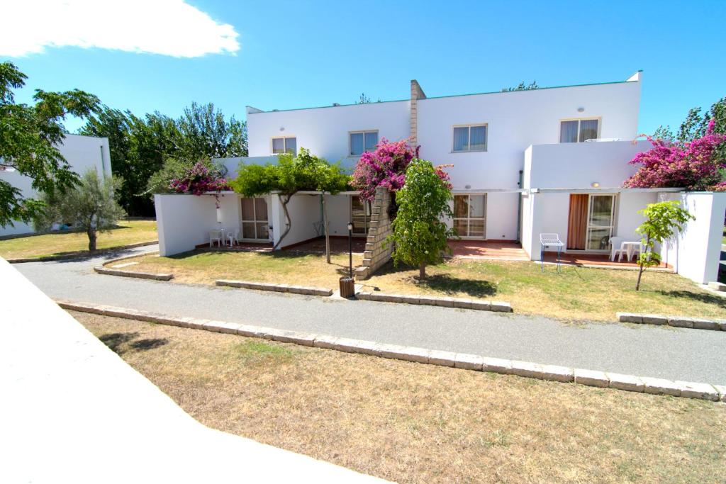 Moderns viesnīcas komplekss ar baltām ēkām, ko ieskauj zaļumi un ziedošas krūmi. Skats uz klusu iekšējo pagalmu, kurā ir sēdvietas un pastaigu celiņi.