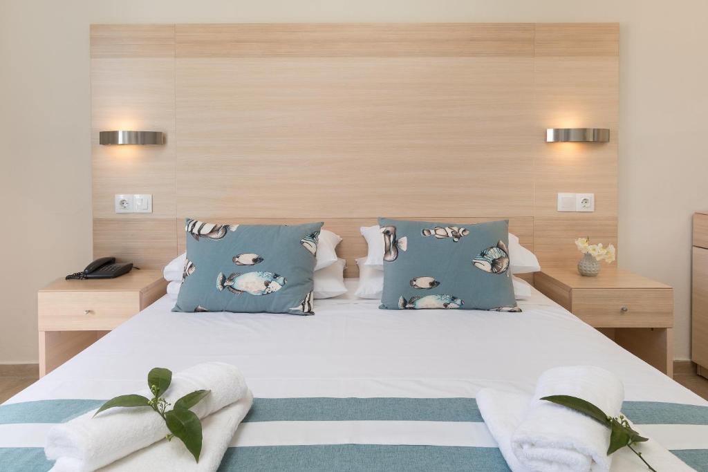 Mūsdienīga guļamistaba ar gultu, dekoratīviem spilveniem ar zivju motīviem un siltu koka apdari. Blakus gultai redzamas naktslampas un neliela puķu kompozīcija.