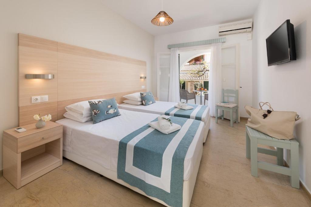 Mūsdienīga viesnīcas numura interjers ar divām gultām, baltiem palagiem un zilu dekori. Numurā ir televizors, naktsgaldiņš ar puķēm un pieeja uz terasi.