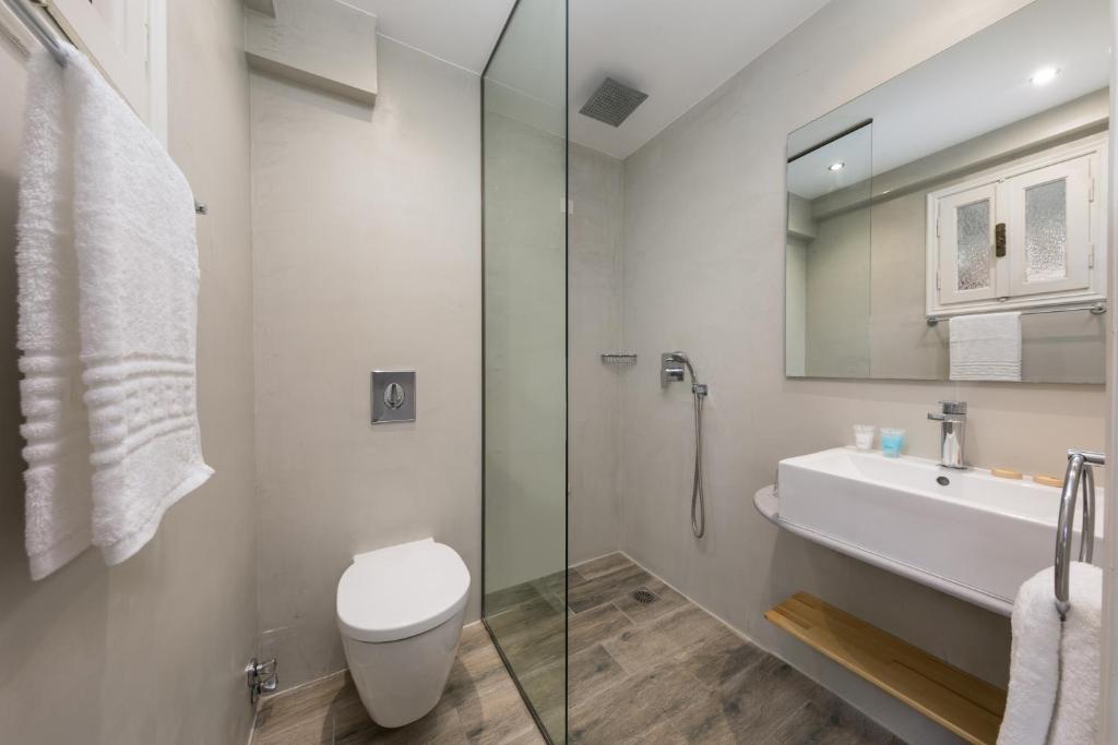 Mūsdienīgs vannas istabas interjers ar stikla dušu, gaišām sienām un minimālisma stilu. Vannas istaba ir aprīkota ar mūsdienīgu izlietni un koka plauktu.