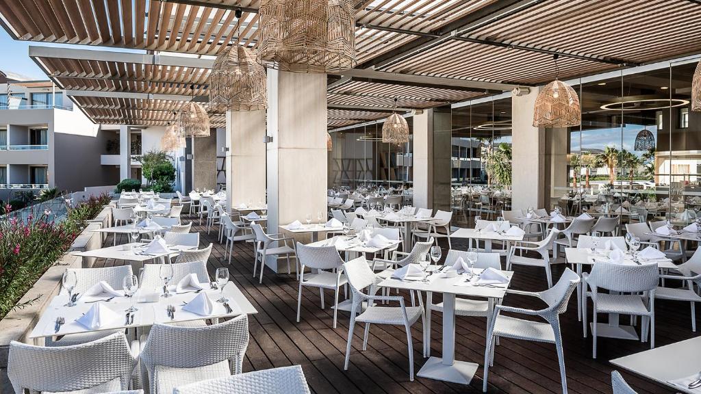 Moderns restorāns ar āra terasi, kurā ir balti galdi un krēsli, grezni galda piederumi un mūsdienīga apgaismojuma elementi. Terase ir apzaļumota un piedāvā patīkamu atmosfēru.