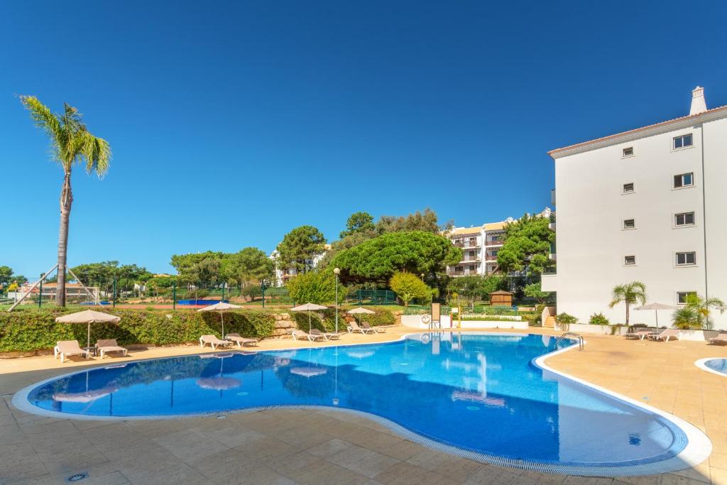 AP Victoria Sport & Beach Hotel āra baseins ar atpūtas krēsliem un skatu uz tenisa kortiem fonā.