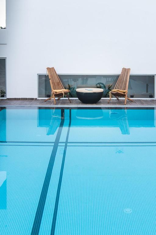 Mūsdienīgs peldbaseins ar divām koka krēsliem un apaļu galdiņu, kas atrodas blakus. Ūdens ir dzidrs un spīdīgs, radot relaksējošu atmosfēru.