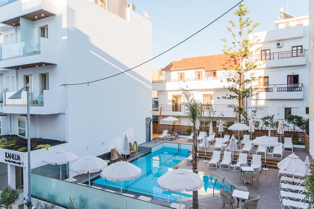 Mūsdienīgas viesnīcas iekšējs pagalms ar peldbaseinu un sauļošanās vietām, kurās ir baltas saulessargu un atpūtas krēsli. Apkārt ir zaļumi un modernas ēkas.