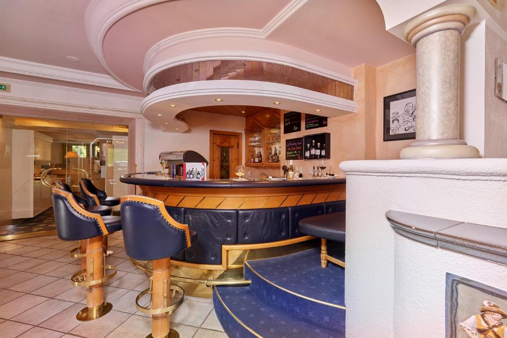 Elegants bārs ar stilīgām krēslām un izsmalcinātu interjeru, kas piedāvā relaksējošu atmosfēru. Bāra letes aizmugurē redzami dzērienu plaukti un melnas tāfeles ar piedāvājumu.