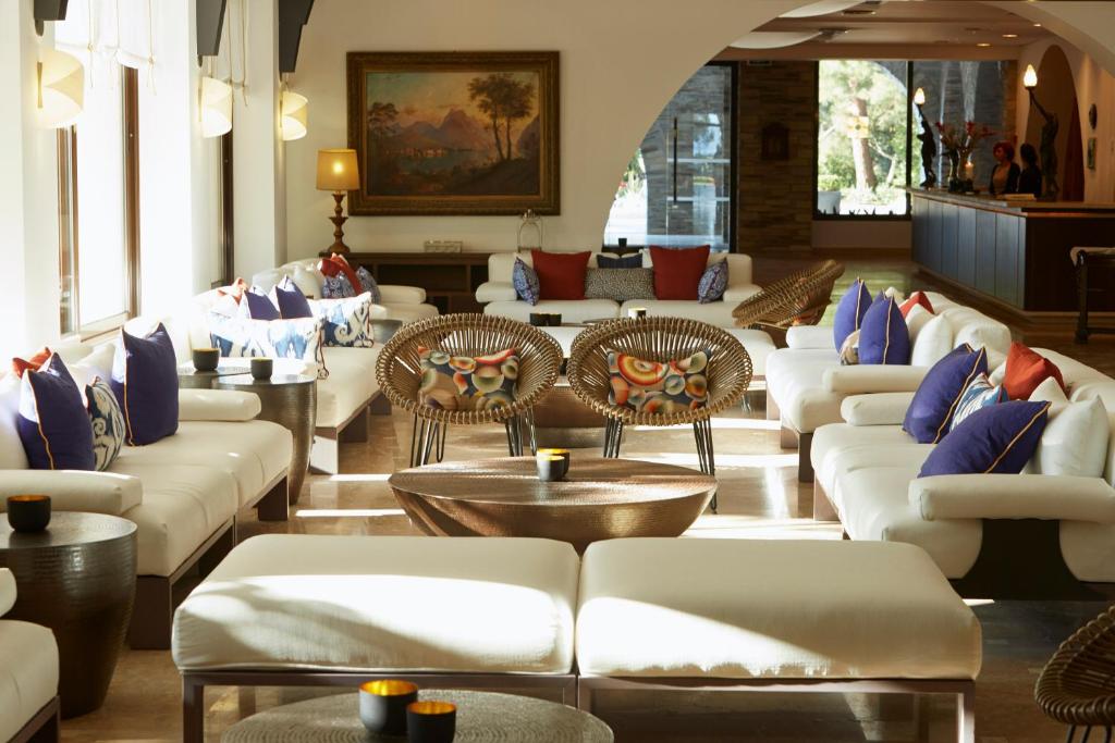 Mūsdienīgs viesnīcas atpūtas telpas interjers ar ērtiem dīvāniem un spilveniem, kas izveidots relaksējošai atmosfērai. Gaisma plūst cauri logiem, radot siltu un viesmīlīgu noskaņu.