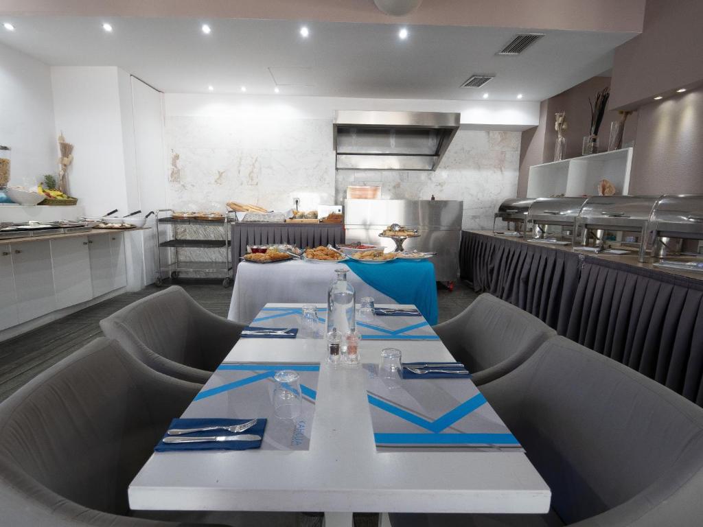 Mūsdienīgs restorāns ar stilīgu interjeru, kurā redzama ēdienu bufete un eleganti galdi ar sudraba galda piederumiem.