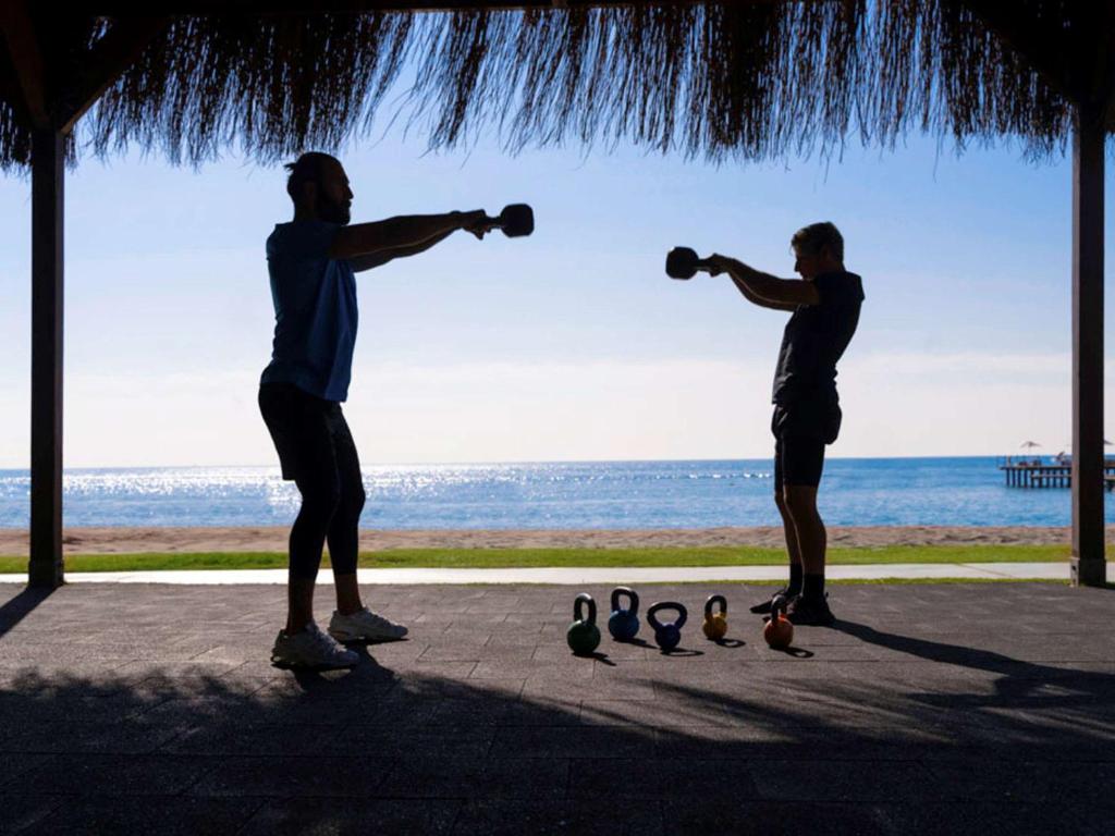Divi cilvēki vingro, izmantojot kettlebell pie Rixos Premium Belek piekrastes.