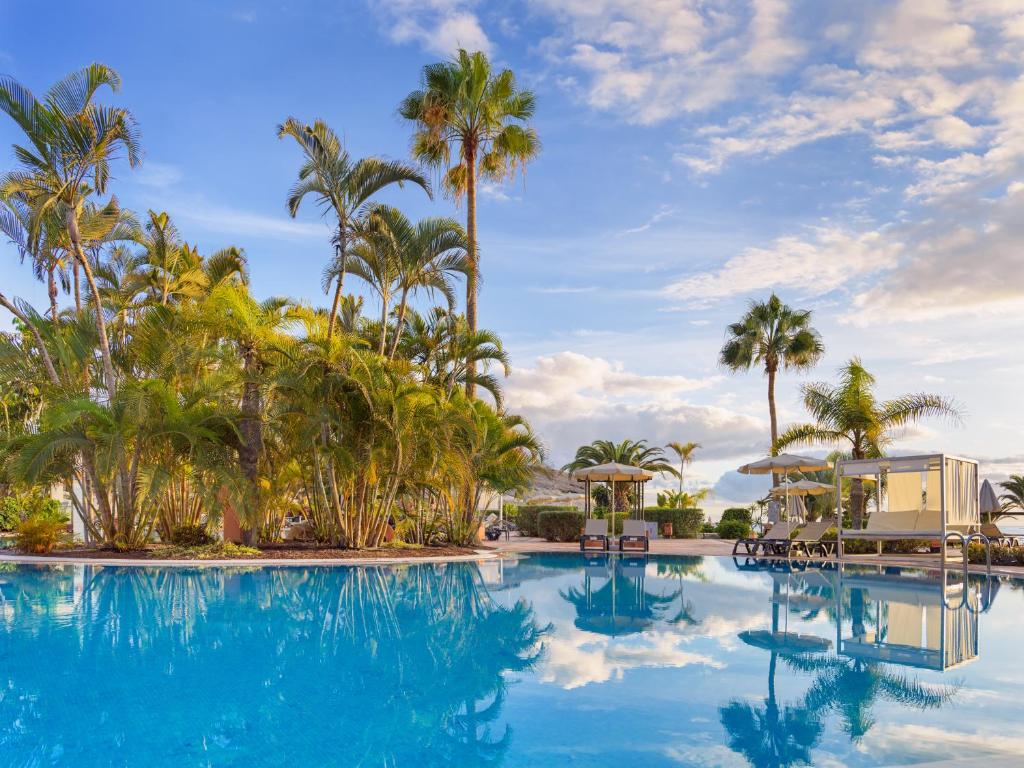 Tropu ainava ar skaidru zilu baseinu un palmu kokiem, kas atspoguļojas ūdenī. Ideāla vieta atpūtai un relaksācijai.