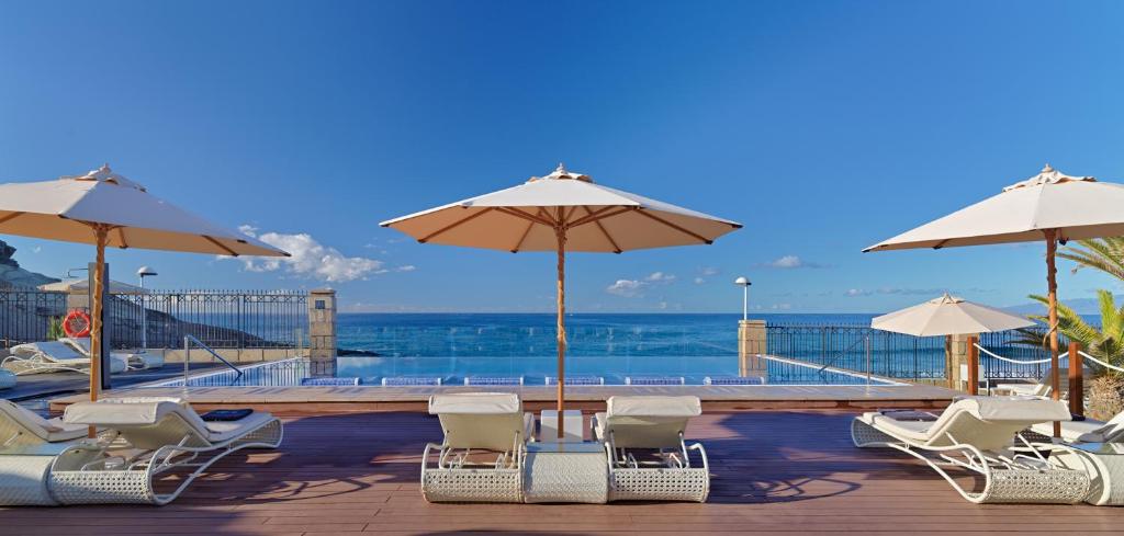 Peldbaseins ar saulessargiem, kas atrodas pie jūras, ar skatu uz mierīgu ūdeni un skaidru debesu. Ideāla vieta relaksācijai un atpūtai.