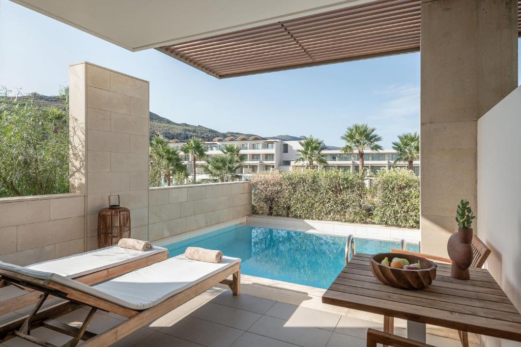 Mūsdienīgs terases skats ar privātu baseinu un atpūtas zonu, kurā ir sauļošanās krēsli un koka galds ar augļiem. Apkārt aug zaļi palmu koki un ainaviska daba.